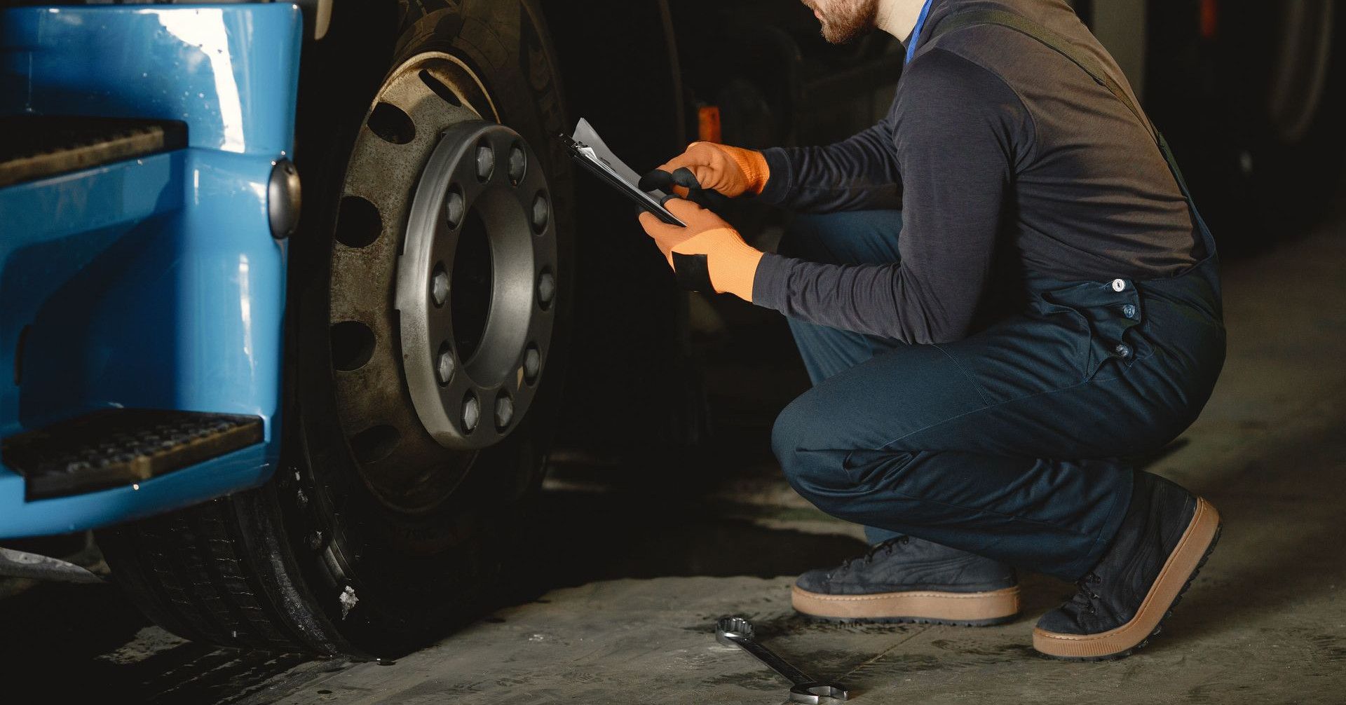 Mechanic checking a truck's wheel using a tablet in an indoor garage setting.